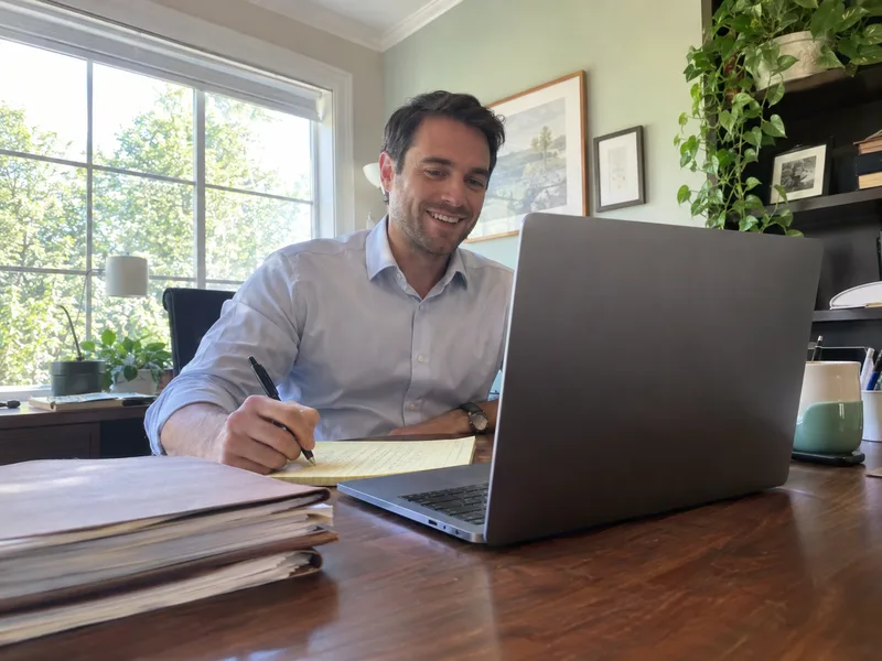 An attorney smiling on a client video call while taking notes.