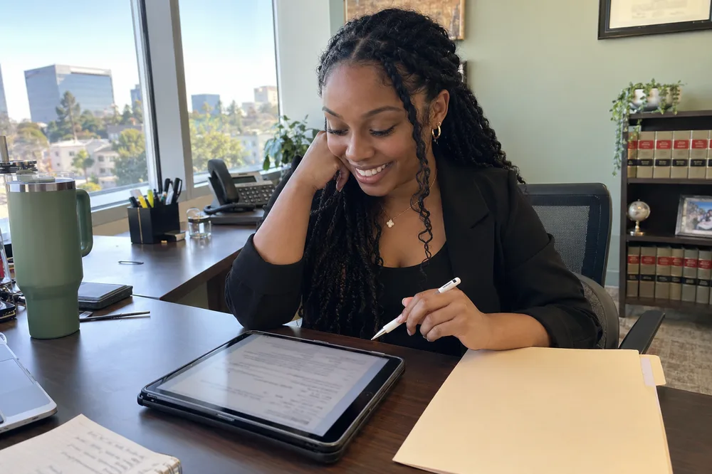 A paralegal smiling at a tablet with a completed intake form, a new client folder beside her.